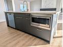 Kitchen island with stainless steel microwave, dishwasher, gray cabinets, and light countertops at 2280 S Pampa Ave, Pahrump, NV 89048