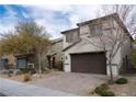 Beige two-story home featuring a brown two-car garage, a brick driveway and desert landscaping at 2240 Sky Island Dr, Henderson, NV 89002