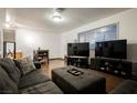 Open living room with wood floors, gray sofa, large window, and three large televisions at 271 Greenbriar Townhouse Way, Las Vegas, NV 89121
