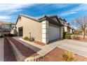 Exterior view of a home showcasing a two-car garage, neutral stucco, and low-maintenance desert landscaping at 523 Painted Cloud Pl, Las Vegas, NV 89144