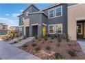 Modern gray townhome featuring a desert landscape, concrete steps, and a bright yellow front door at 332 Pacific Sparrow Ave, Henderson, NV 89011