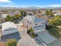 Aerial view of a two-story home with a spacious driveway, detached garage, lush lawn, pool, and mountain views at 9435 Westwind Rd, Las Vegas, NV 89139