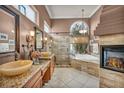 Elegant bathroom featuring dual sinks, a glass shower, a soaking tub and a stone fireplace at 2107 Eaglepath Cir, Henderson, NV 89074