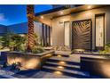 Beautiful modern home featuring an illuminated front entrance, lush landscaping, and stylish details at 678 Blackrock Rim Dr, Henderson, NV 89012