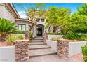 Elegant home entrance featuring stone pillars leading to a grand arched doorway and manicured greenery at 9825 Glenrock Dr, Las Vegas, NV 89134