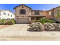 Tan two-story home with a concrete driveway, desert landscaping, and a covered front porch entry at 774 Wigan Pier Dr, Henderson, NV 89002