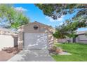 A one-car garage has a manicured lawn, lush trees, and tidy landscaping for a charming curb appeal at 2136 Velvet Hill Ave, Las Vegas, NV 89106