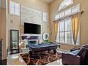 Bright living room featuring a stone fireplace, large windows, pool table, and comfortable seating at 9616 Grand Isle Ln, Las Vegas, NV 89144