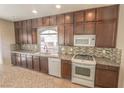 Kitchen features dark cabinets, stone countertops, mosaic tile backsplash and white appliances at 9870 Giant Steps Ct, Las Vegas, NV 89141