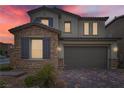 Dusk view of a two-story home showcasing a stone exterior, brown shutters, and a two-car garage at 8125 Skye Vineyard Dr, Las Vegas, NV 89166