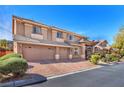 Two-story home with a brick driveway leading to a three-car garage, complemented by mature landscaping at 5868 Revital Ct, Las Vegas, NV 89131