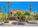 Inviting two-story stucco townhome with a garage, stone accents, and lush, mature landscaping at 65 Luce Del Sole # 1, Henderson, NV 89011