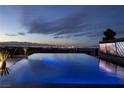 Infinity edge pool with glowing lights overlooking the Las Vegas cityscape at dusk, set against a cloudy evening sky at 811 Magnum Cliff Ct, Henderson, NV 89012