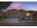 Charming single-story home featuring stone accents, desert landscaping, and an attached two-car garage at twilight at 10746 Lightning Sky St, Las Vegas, NV 89179