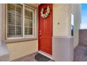 Close-up of a bright red front door with a decorative wreath and sidelight window at 10556 Nantucket Ridge Ave, Las Vegas, NV 89166