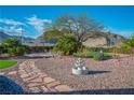 Landscaped backyard featuring a decorative fountain, rock landscaping, and mature trees against a mountain backdrop at 10716 Bennington Ct, Las Vegas, NV 89134