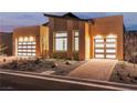 Striking home exterior with a modern design, landscaped yard, a brick driveway, and two-car garage, beautifully illuminated at 10739 Agate Cliffs Ave, Las Vegas, NV 89135