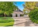 View of the brick two-car garage with an upper story and paved driveway and mature trees at 3001 Astoria Pines Cir, Las Vegas, NV 89107