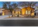 Inviting single-story home with stone accents, warm lighting, and landscaped front yard at dusk at 7307 Iron Oak Ave, Las Vegas, NV 89113
