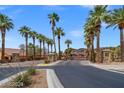 A long, paved street lined with palm trees leads to a gated entry under a clear sky at 33 Via Di Mello, Henderson, NV 89011