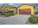 Wide driveway leading to a two-car garage, complemented by lush, round shrubs in the front yard at 10632 Open Range Ct, Las Vegas, NV 89179