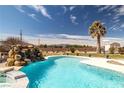 Beautiful backyard showcasing a pool with a rock waterfall, complemented by desert landscaping and mountain views at 671 W Hickory St, Pahrump, NV 89048