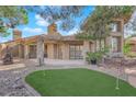Landscaped backyard with a putting green, gravel, covered patio, and mature trees, creating a relaxing outdoor space at 7368 Mission Hills Dr, Las Vegas, NV 89113