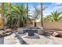 Cozy stone patio area with comfortable seating, a gas fire pit, and tropical palm trees at 124 Beach Oak Ave, Henderson, NV 89002