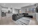 Open-concept living room with modern gray sectional, tile flooring, and an adjacent kitchen area at 3192 Timorasso Ave, Henderson, NV 89044