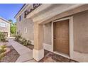 Beige home featuring stucco siding, a brown front door, and well-kept landscaping around the entrance at 1425 Bow Creek Ct, Las Vegas, NV 89128