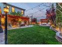 A green, spacious backyard featuring ambient string lighting, a pergola, and an inviting outdoor seating area at 10988 Wonder Hills St, Las Vegas, NV 89141