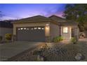 Charming single-story home at dusk, featuring a two-car garage, desert landscaping and warm exterior lighting at 2444 Gamma Ray Pl, Henderson, NV 89044