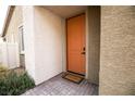 Exterior view of an orange front door framed by textured walls and a welcome mat at 6925 Cuddy Falls Pl, North Las Vegas, NV 89084