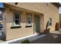 The front of a stucco home shows the door and 2 windows with green trim and stone landscaping at 7731 Ornamento Way, Las Vegas, NV 89179
