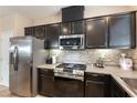 Close-up of kitchen area featuring stainless steel appliances, dark cabinets, and stylish backsplash at 6255 W Arby Ave # 183, Las Vegas, NV 89118