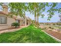 Well-manicured backyard with green lawn, covered patio, mature trees, and views of the surrounding landscape at 138 Wentworth Dr, Henderson, NV 89074