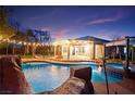 Backyard oasis features a sparkling pool with a rock waterfall, a covered patio with string lights, and a lush garden at 6907 May Basket Ave, Las Vegas, NV 89131