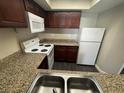 Condo kitchen featuring granite countertops, white appliances, and dark cabinets at 6800 E Lake Mead Blvd # 1018, Las Vegas, NV 89156