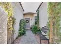 Charming courtyard entry featuring a wrought iron bench, lush greenery, and a decorative wreath on the front door at 10847 Intro Ave, Las Vegas, NV 89135