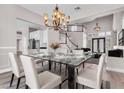 Dining room with modern chandelier, glass table, white chairs and open floor plan at 3088 Via Flaminia Ct, Henderson, NV 89052