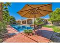 Relaxing backyard featuring a sparkling pool with a large tan umbrella and beautiful outdoor seating at 6527 Lokai Ave, Las Vegas, NV 89130