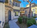 Close-up of a stucco and stone home with an arched doorway, balcony, and desert landscaping at 7695 Windy Meadow Ave, Las Vegas, NV 89178