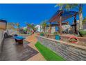 Multi-tiered backyard featuring a pergola, stone retaining wall, artificial turf, dining table, and lounge furniture at 516 Arizona St, Boulder City, NV 89005