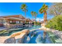 Backyard pool and spa area features rock details, a bar, and swaying palm trees on a clear day at 8348 Mountain Destiny Ave, Las Vegas, NV 89131