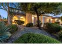 Stunning landscaped front yard with lush green bushes, desert plants, and mature trees at dusk at 7416 Redhead Dr, North Las Vegas, NV 89084