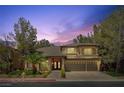 Beautiful two-story home with a three-car garage, landscaped front yard and elegant brick entryway at dusk at 4156 Balmoral Castle Ct, Las Vegas, NV 89141