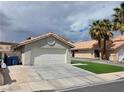 A single-story house featuring a two-car garage, desert landscaping, and mature palm trees at 7091 Rhapsody Ln, Las Vegas, NV 89119