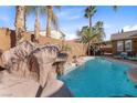 Outdoor pool area with rock waterfall feature and tropical landscaping at 496 Grassrange Ln, Henderson, NV 89052