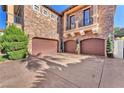 Three car garage with stone accents, manicured bushes, and a paved driveway at 1795 Anelli Ct, Henderson, NV 89012
