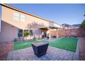 A private backyard with a covered patio, manicured lawn, and a modern fire pit feature at 189 Kings Canyon Court Ct, Henderson, NV 89012